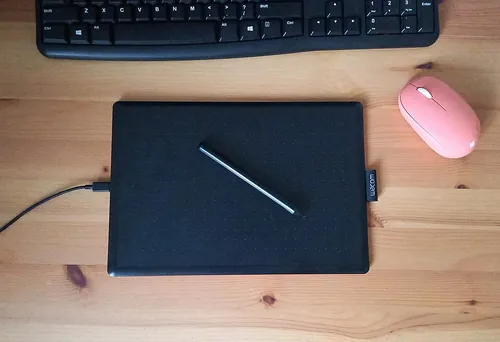 Wacom graphic tablet ("One by Wacom"), pink mouse and a keyboard on a wooden desk,